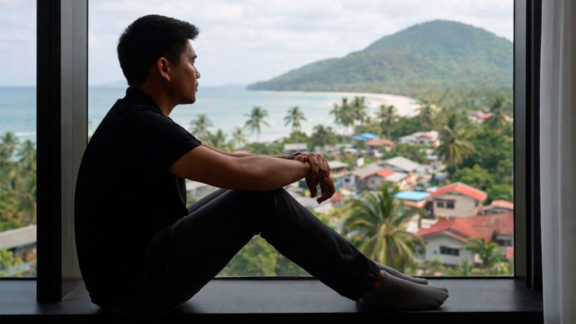 A Filipino man sitting by a window looking outside, reflecting on signs you haven’t moved on from your first love.