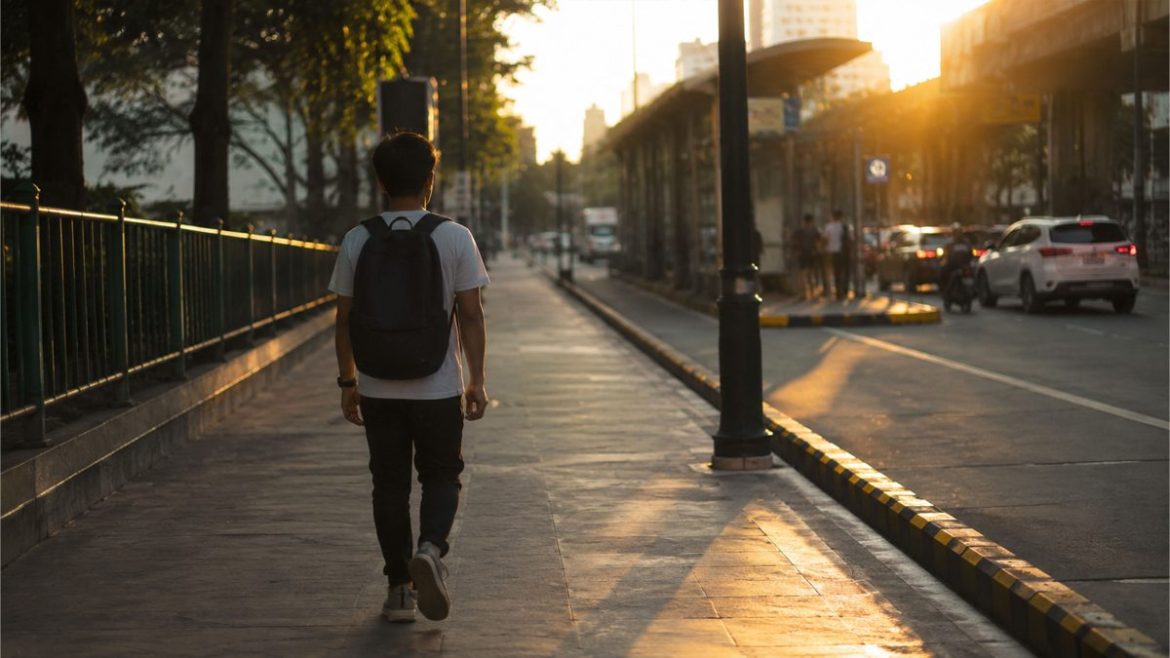 Young Filipino man walking along a city sidewalk during golden hour in Metro Manila