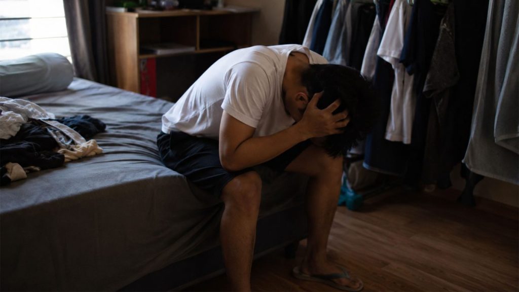 Young Filipino man sitting alone in his room feeling emotionally overwhelmed