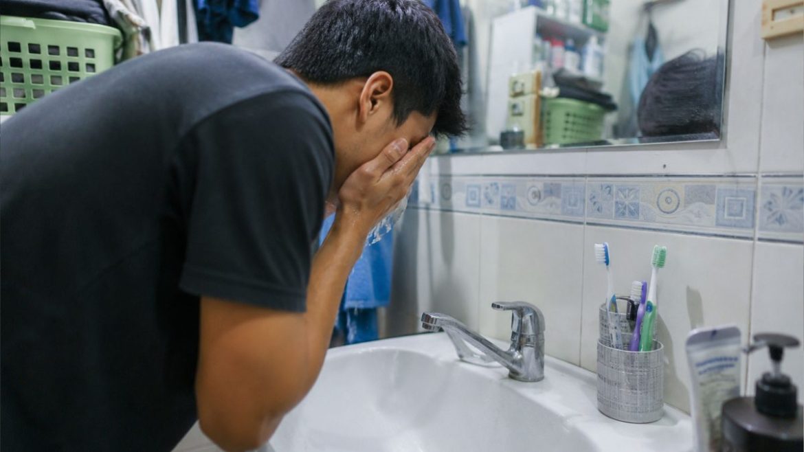 Filipino man washing his face in a bathroom while practicing daily hygiene habits