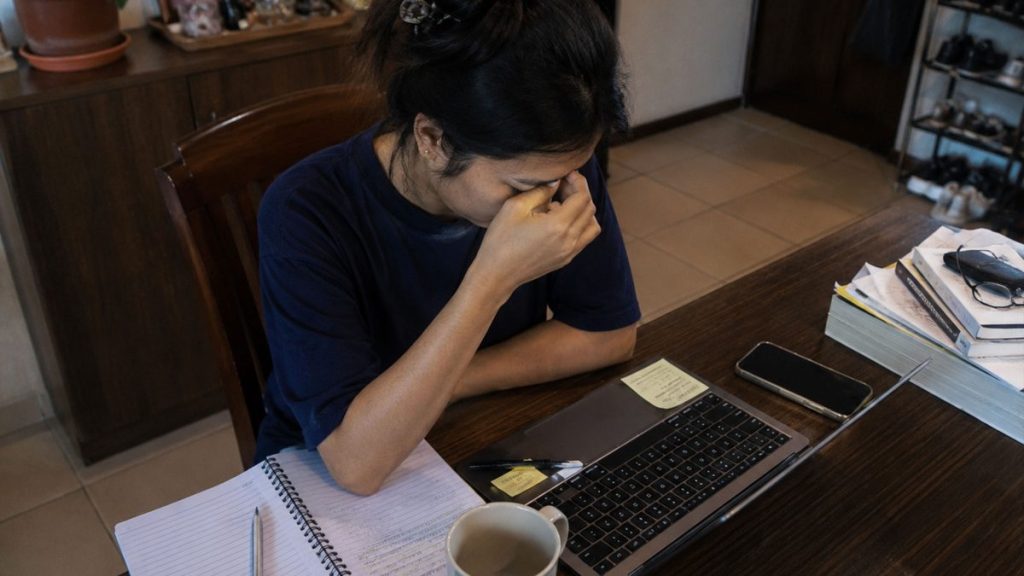Filipino woman sitting at a desk feeling overwhelmed while working remotely