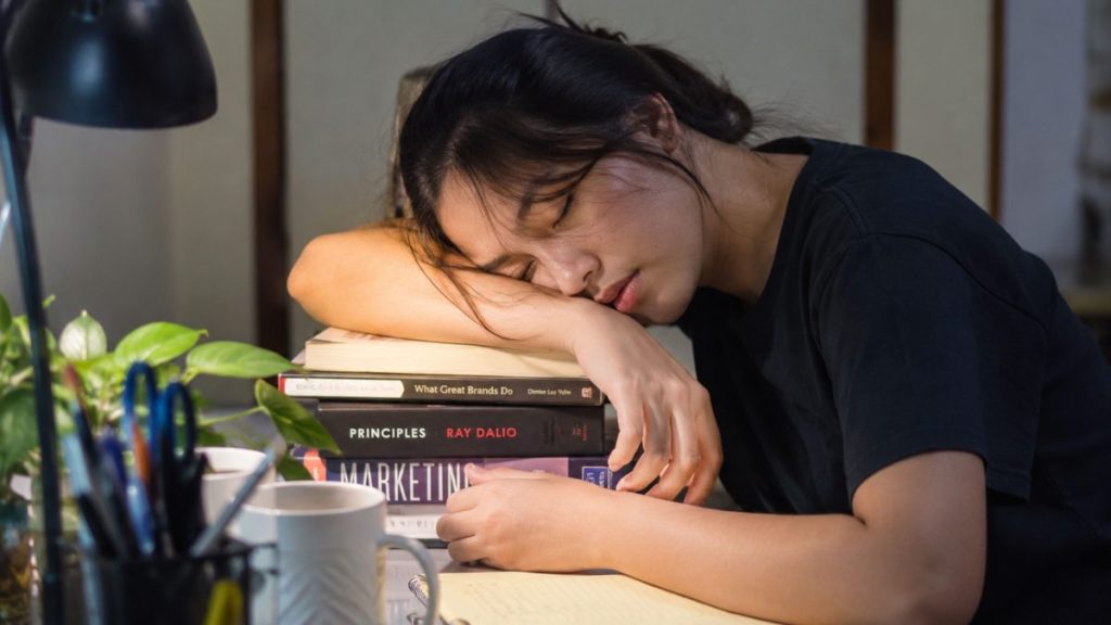 Tired Filipina student resting on books during late-night studying