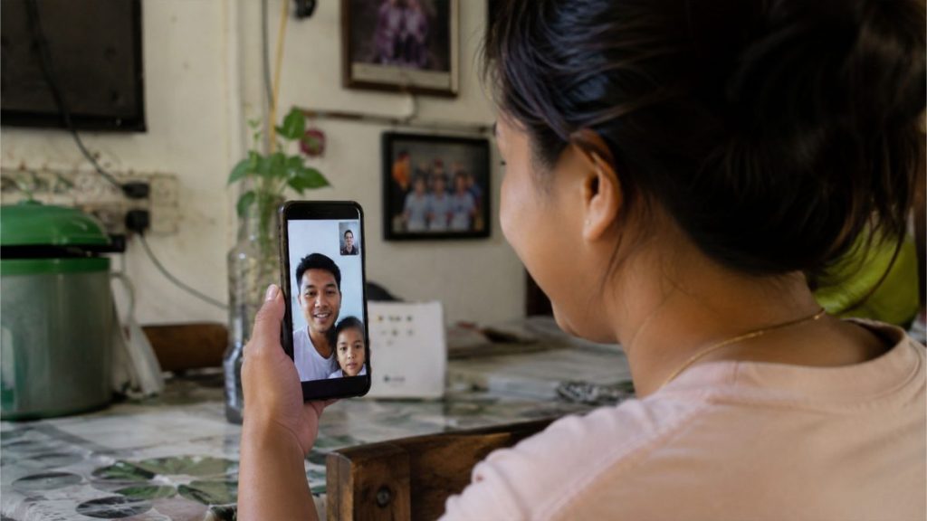 Filipino woman video calling her husband and child while managing family life during overseas employment.