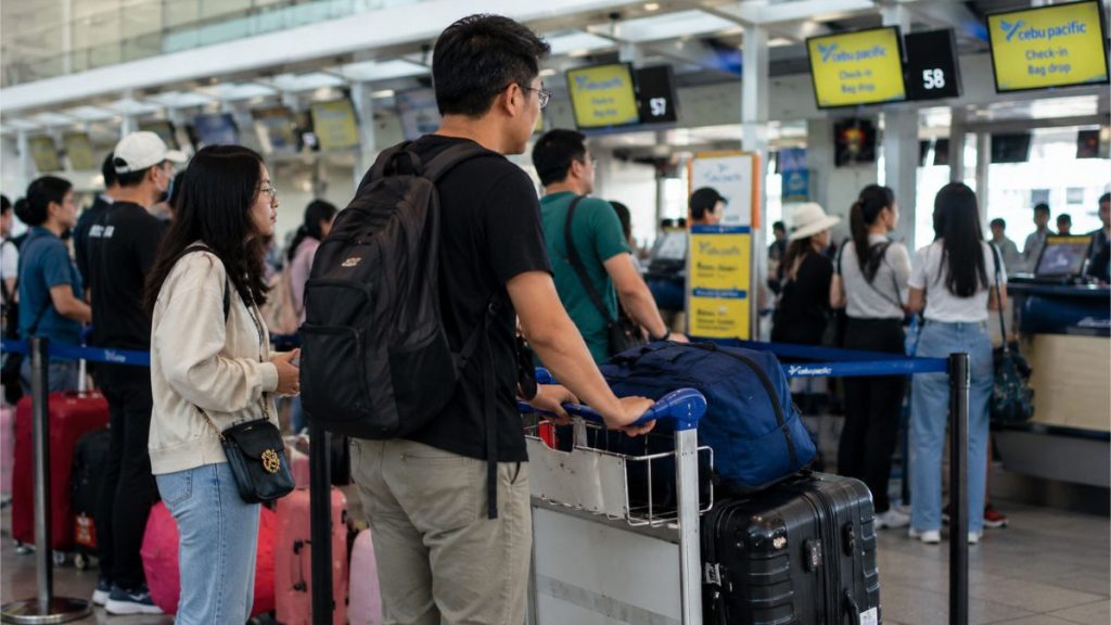 Filipino travelers waiting in line at airport check-in counters with luggage.