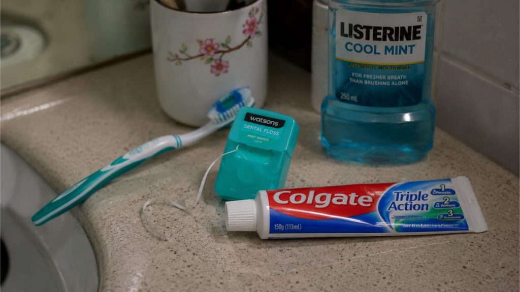Toothbrush, toothpaste, floss, and mouthwash arranged on a bathroom counter