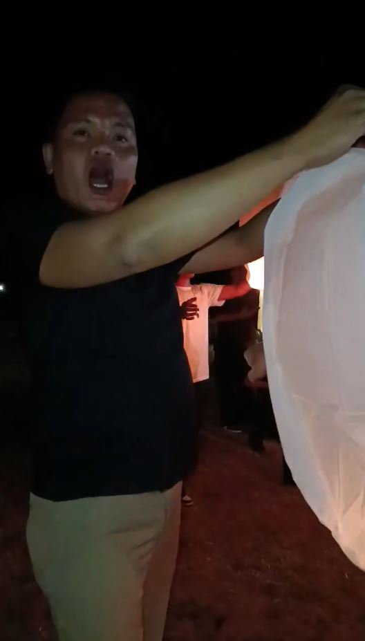 A man releases a glowing sky lantern during a nighttime gathering in a viral Filipino celebration video.