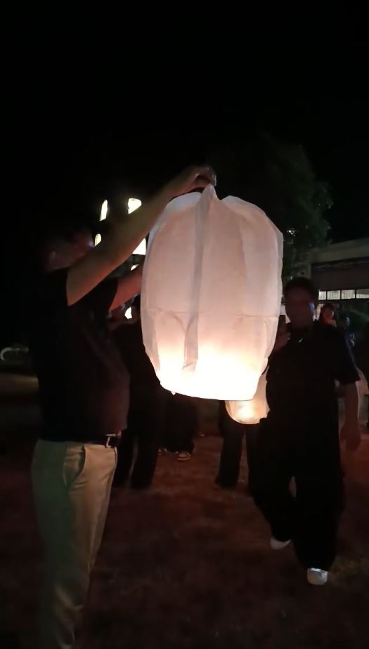 People gather outdoors at night while releasing glowing sky lanterns during a viral celebration moment.