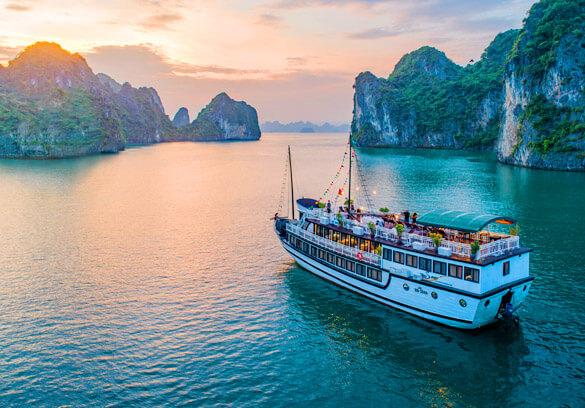 Tourist cruise navigating the emerald waters and limestone islands of Bai Tu Long Bay, Vietnam.