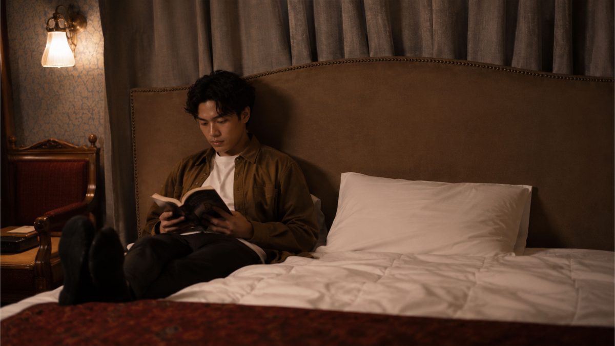 Filipino man reading a book while sitting comfortably in bed under warm bedroom lighting.
