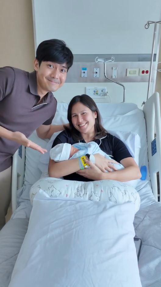 Maiqui Pineda cradles her newborn baby while Robi Domingo stands beside her in a hospital room.