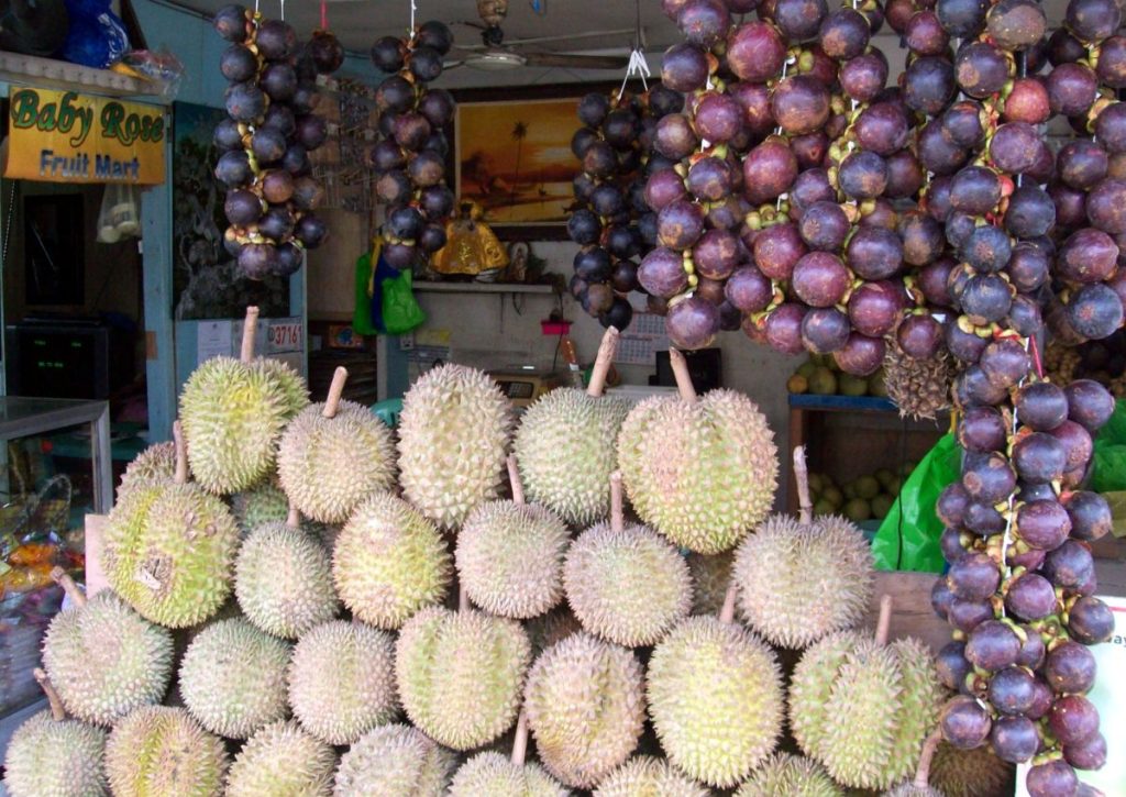 Durians displayed at a fruit market during durian season alongside other tropical fruits.