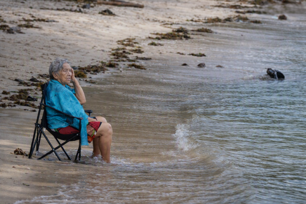 An elderly woman sitting by the shoreline, representing aging and the importance of osteoporosis therapy for maintaining bone health.